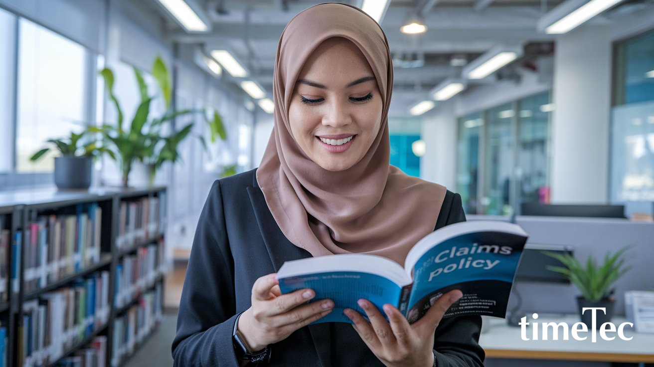 A woman in a hijab reading a book in an office setting, symbolizing understanding claims policies in Malaysia.