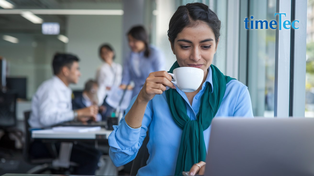 Malaysian woman drinking coffee while working on a payroll management system on her laptop