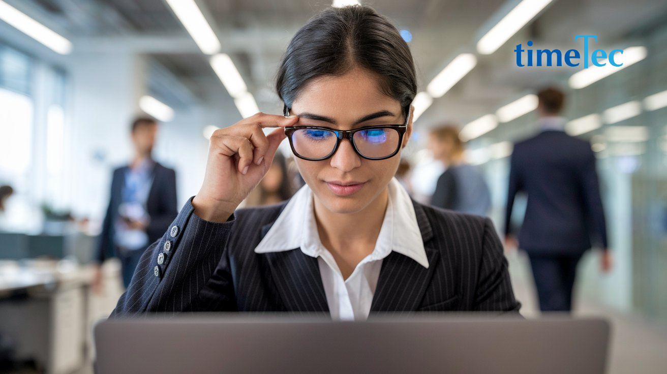 Focused businesswoman wearing glasses, working on a laptop in a modern office.