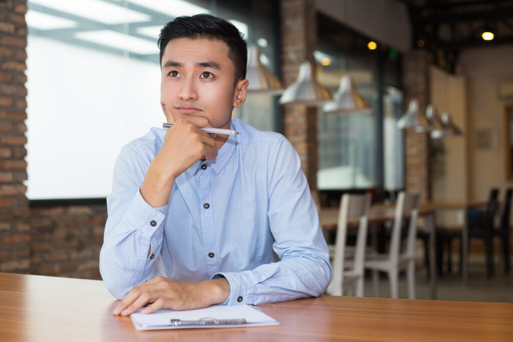 Young businessman in a cafe, thoughtfully planning with a clipboard, representing the process of creating a claims policy for small companies.