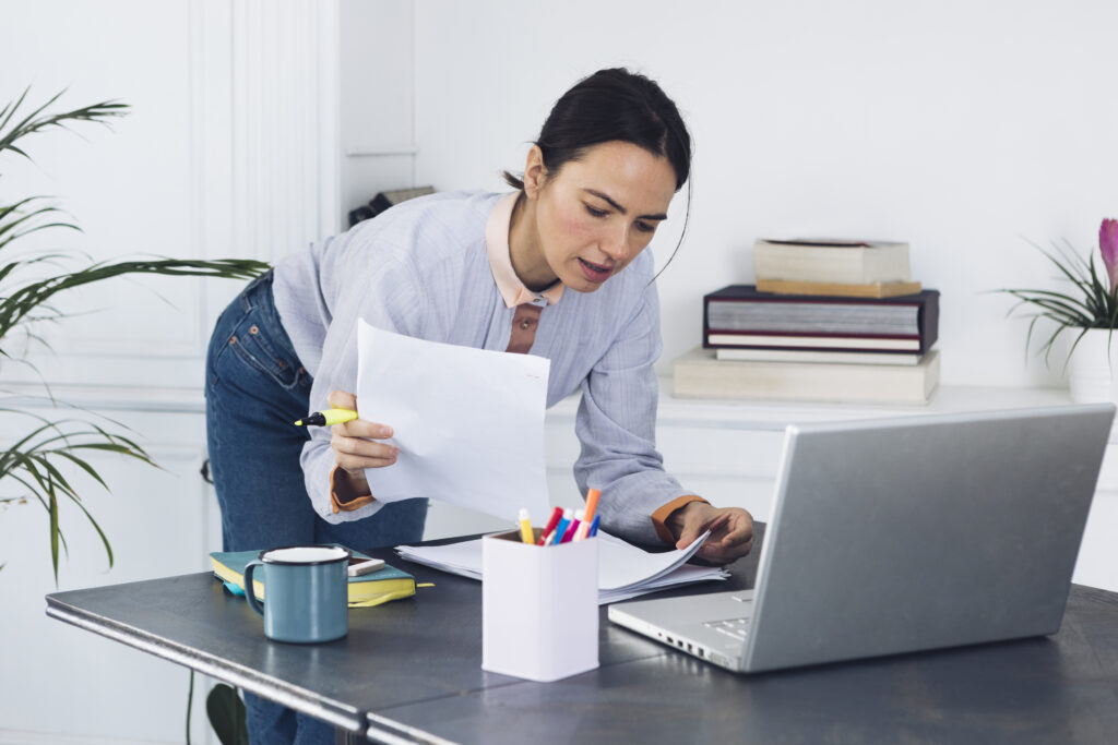 Woman reviewing documents and using a laptop to address common payroll challenges