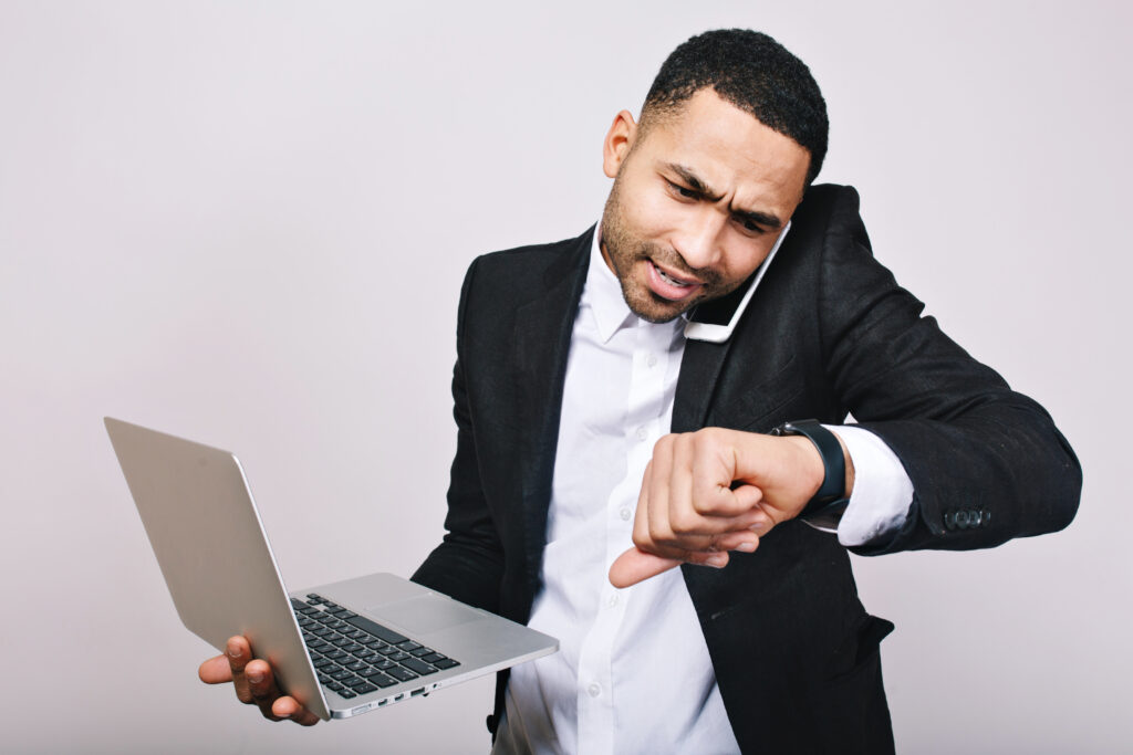 Busy businessman checking his watch while talking on the phone and holding a laptop, ensuring he has made all the payments on time.