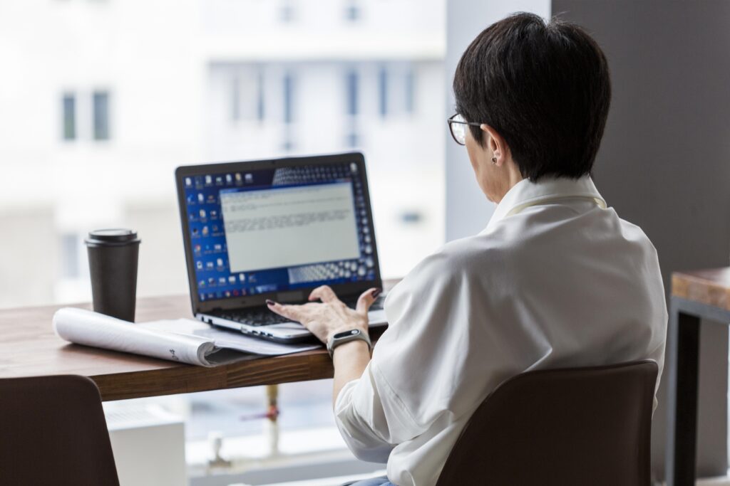 Businesswoman working on a laptop with a coffee cup and documents on the desk streamlining payroll processes with automation.