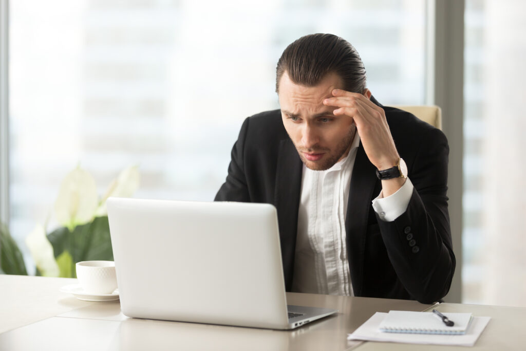 Upset businessman looking at laptop screen, feeling stressed about work-related issues.