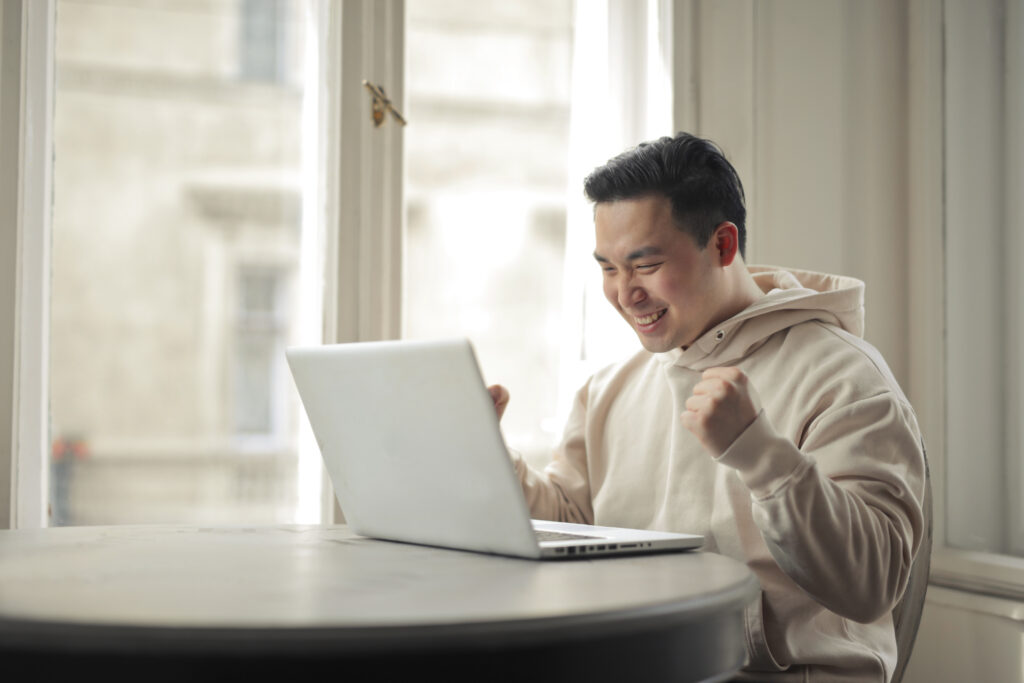 Young businessman celebrating success in front of his laptop, symbolizing the benefits of payroll software.