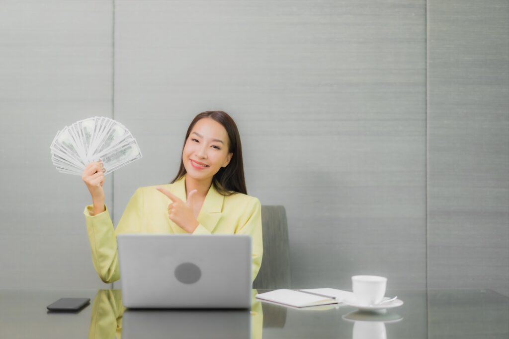 Young Asian businesswoman holding cash and pointing, representing cost management and the importance of accurate attendance tracking in Malaysia