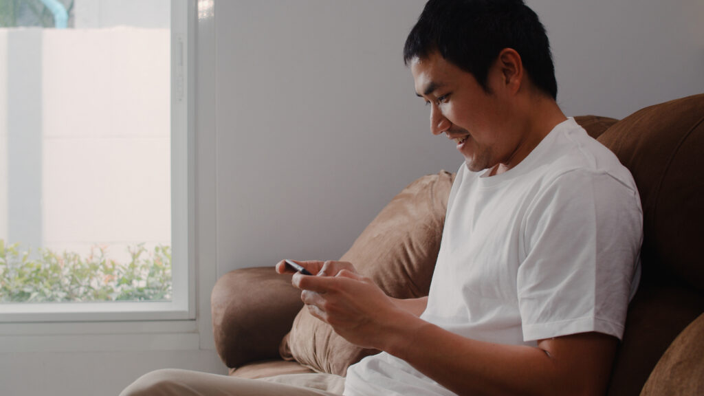 Man using a mobile app on his smartphone while relaxing at home.