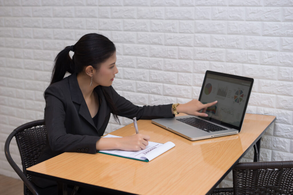 A young businesswoman in a suit pointing to audit data on a laptop, reviewing attendance management system effectiveness.