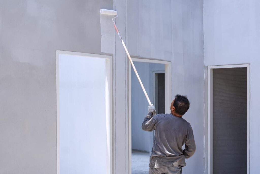 A builder applying primer on an indoor wall as part of residential maintenance.