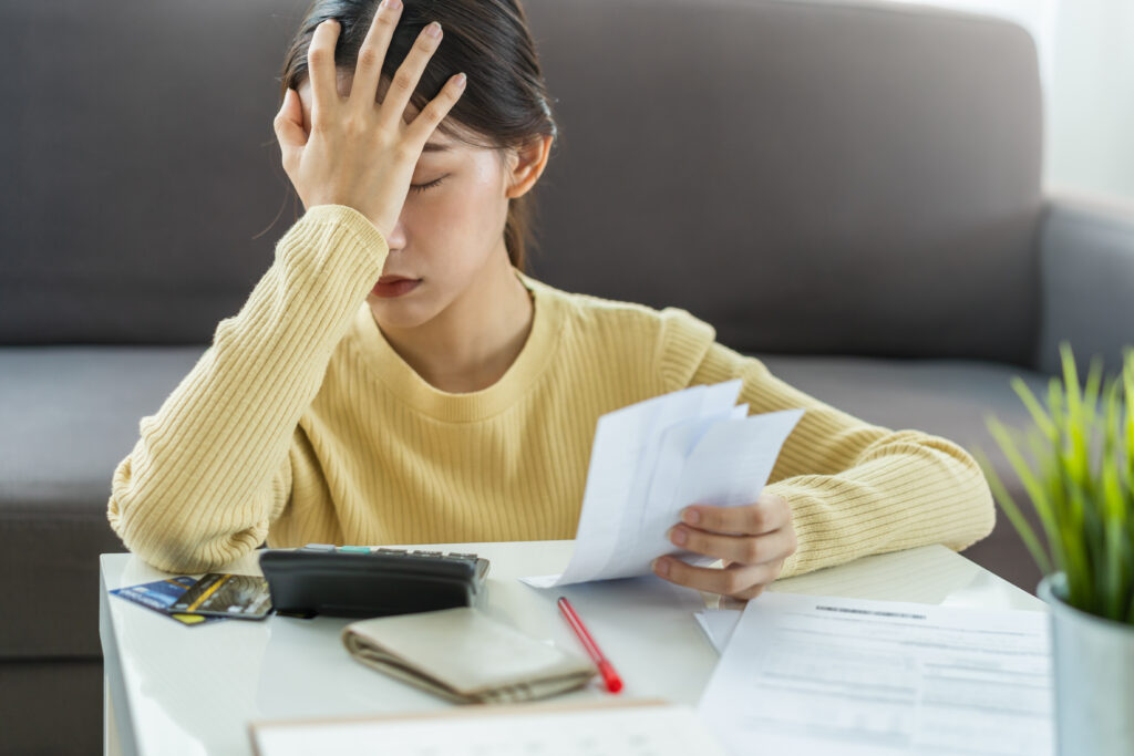 A woman sitting at a table, stressed while calculating monthly bills and expenses.