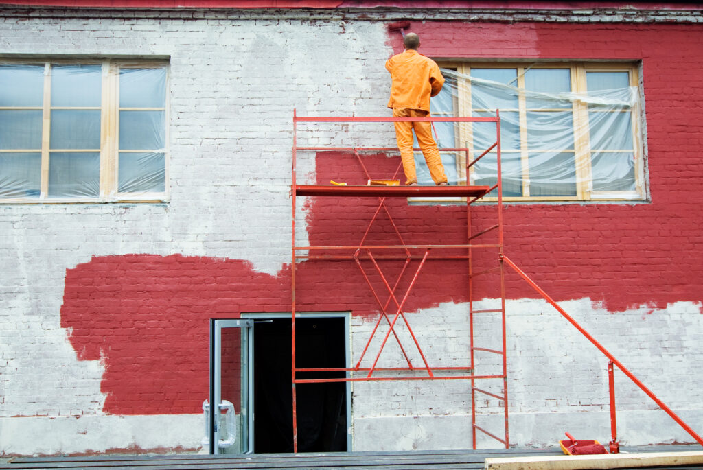 Worker painting a building red on scaffolding, a project funded by sinking funds.