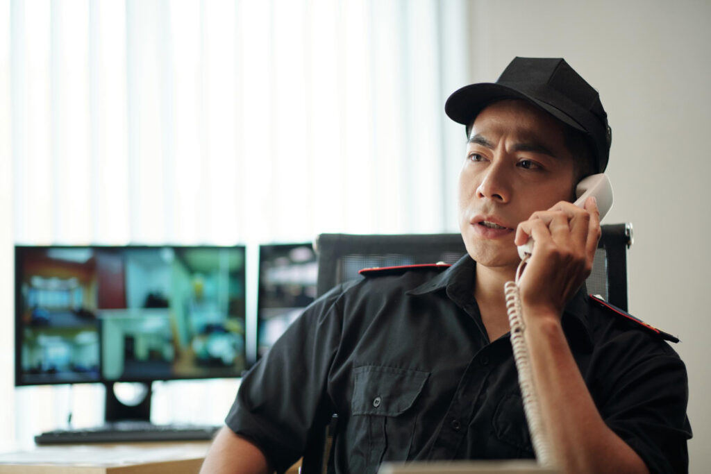 Security guard communicating through a landline phone in front of security monitors.